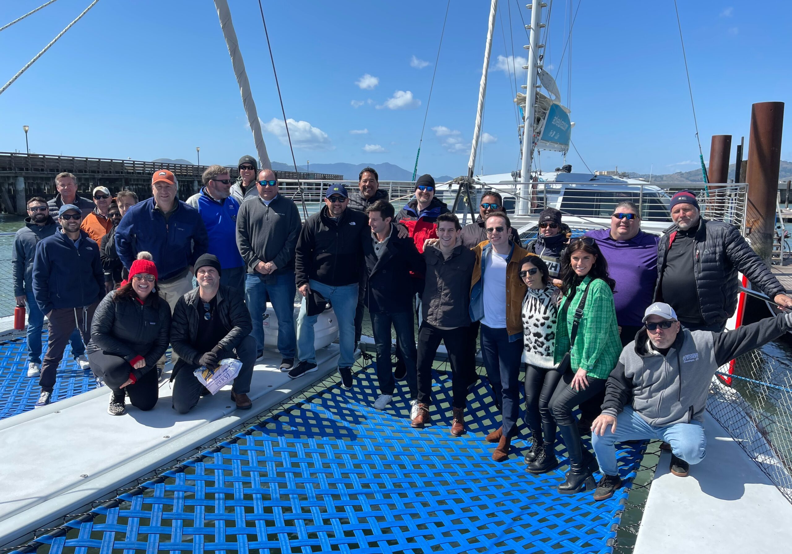group of professionals standing on the netting of the Adventure Cat catamaran, smiling. Beautiful sunny day with blue skies.