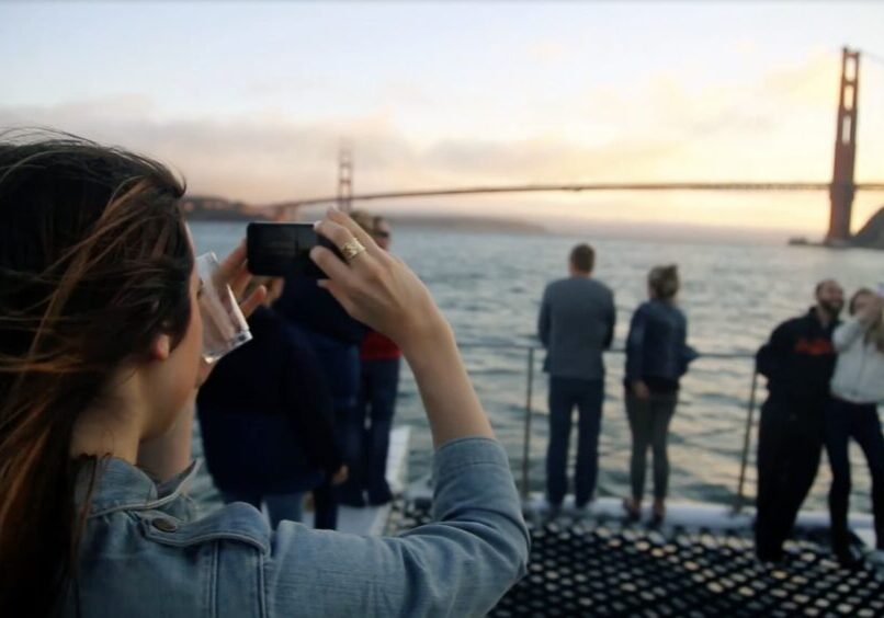 A tourist takes a photo of the Golden Gate Bridge with her cell phone while sailing on the bay.